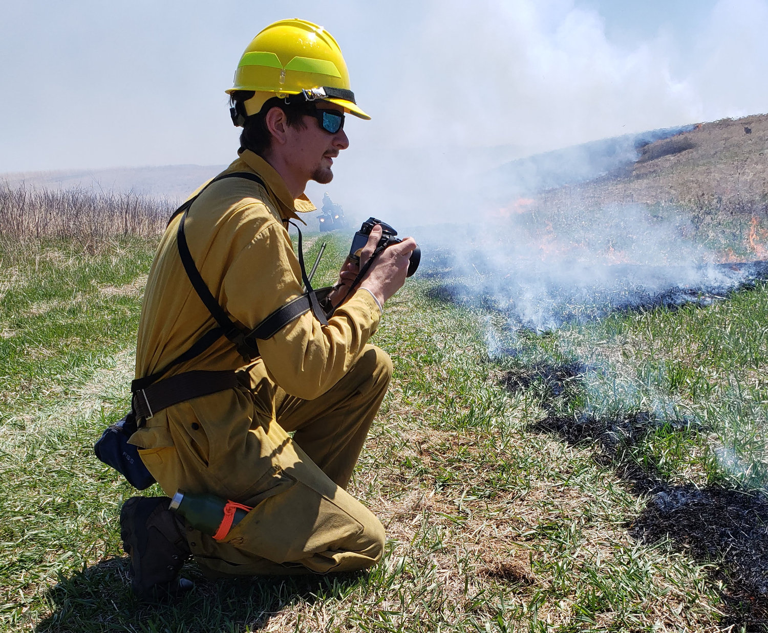Man in fireproof outfit taking photographs at a prairie burn