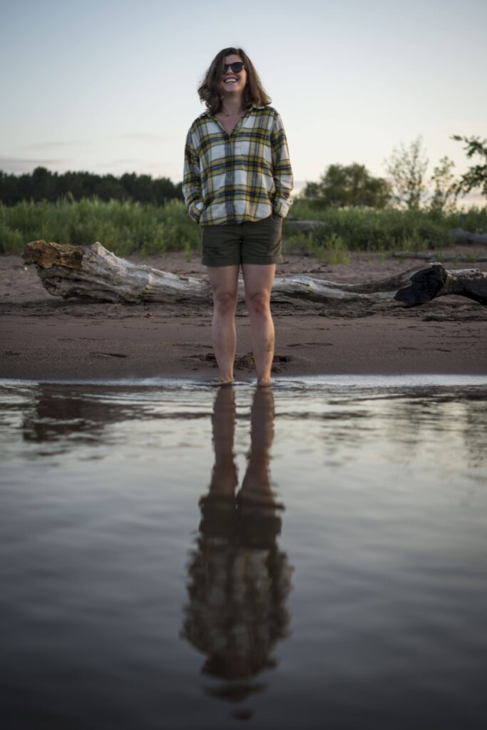 A person standing at the edge of water with their reflection showing.